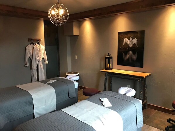 Une chambre avec deux lits, un banc, un téléviseur fixé au mur et un tableau.