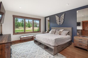 A bedroom with a large bed, wooden bench, and a window with a view of trees. - Modern-Rustic Retreat + Full Kitchen, Soaking Tub, Office, Media Room & Deck (Whitefish)