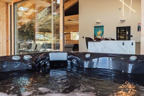 A hot tub with a wooden interior, a glass wall with a view of trees, and a bar area with a poster on the wall. - Chalet Eteila with Sauna, Jacuzzi and Cinema (Combloux)