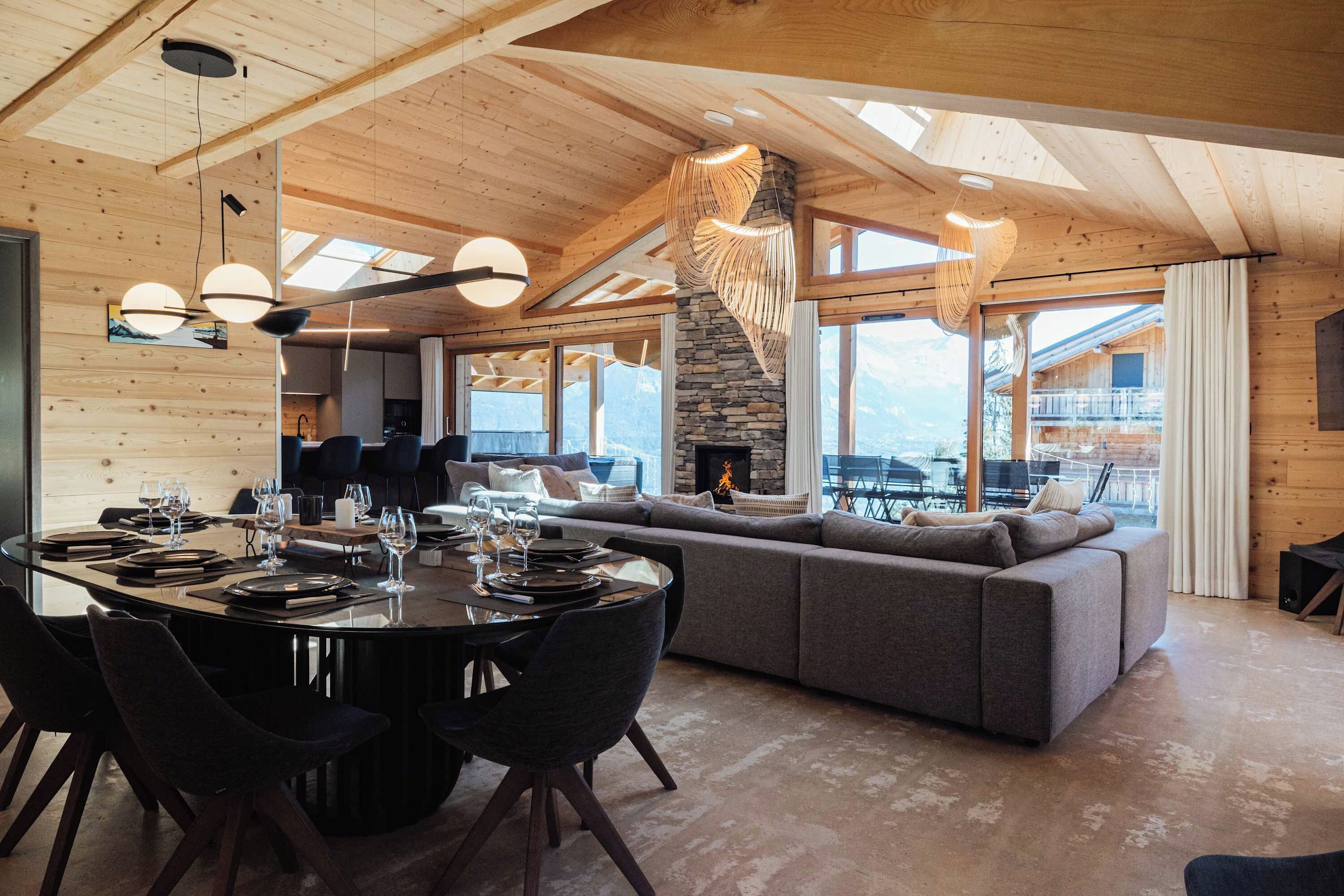 A spacious living area with a large wooden ceiling, a stone fireplace, and a view of the mountains.