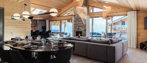 A spacious living area with a large wooden ceiling, a stone fireplace, and a view of the mountains.