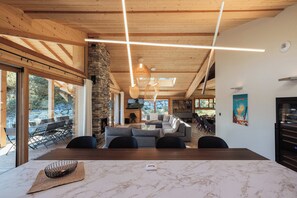 A modern interior with a stone fireplace, a large dining table, and a cozy seating area. - Chalet Eteila with Sauna, Jacuzzi and Cinema (Combloux)