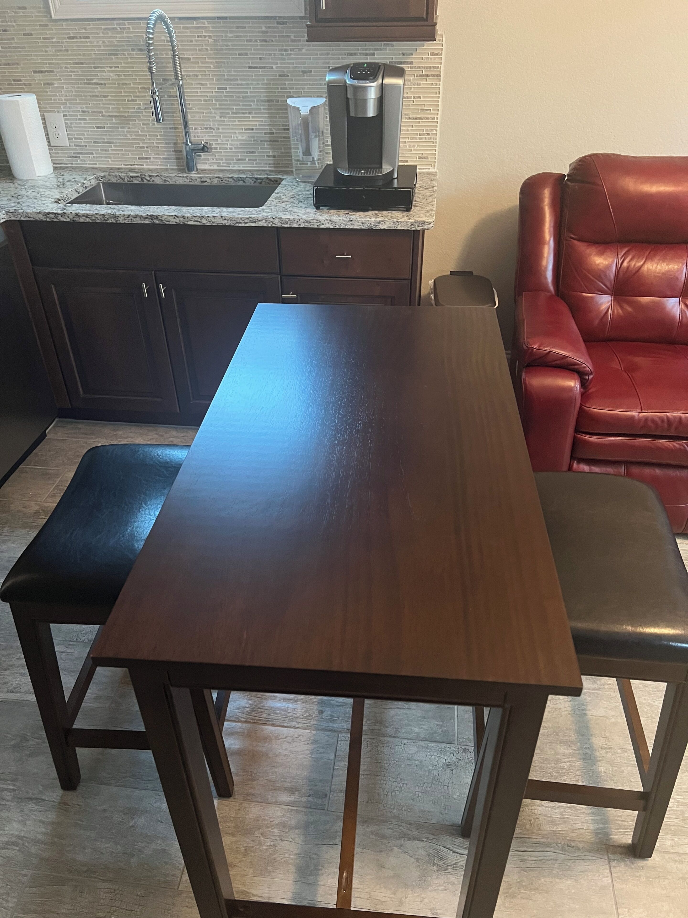 A kitchen with a stainless steel sink, a coffee maker, and a red leather chair.
