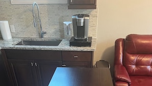 Una cocina con un lavamanos de acero inoxidable, una cafetera y un sillón de cuero rojo.