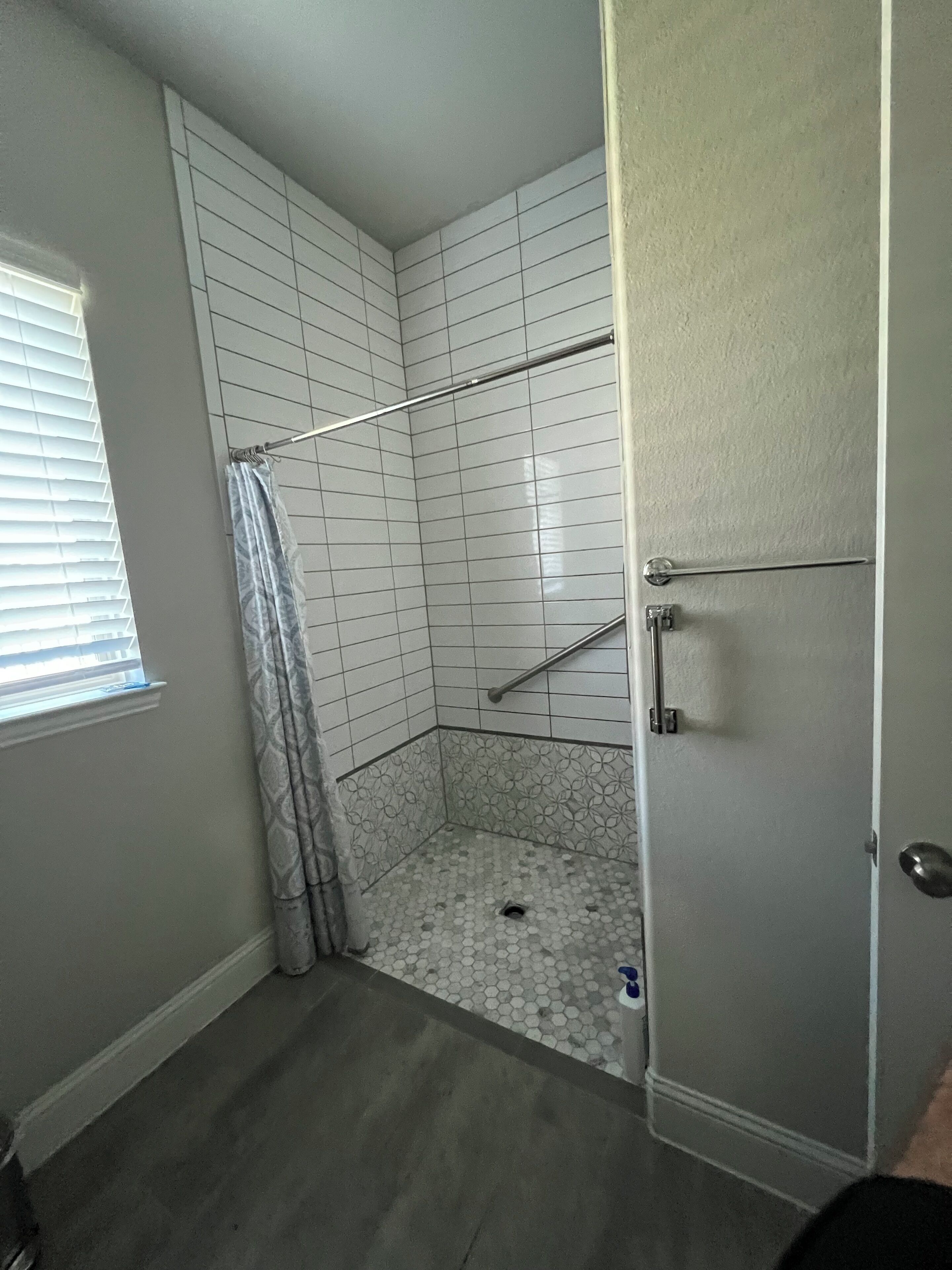 A small, enclosed shower area with a shower curtain, a handrail, and a tiled floor.