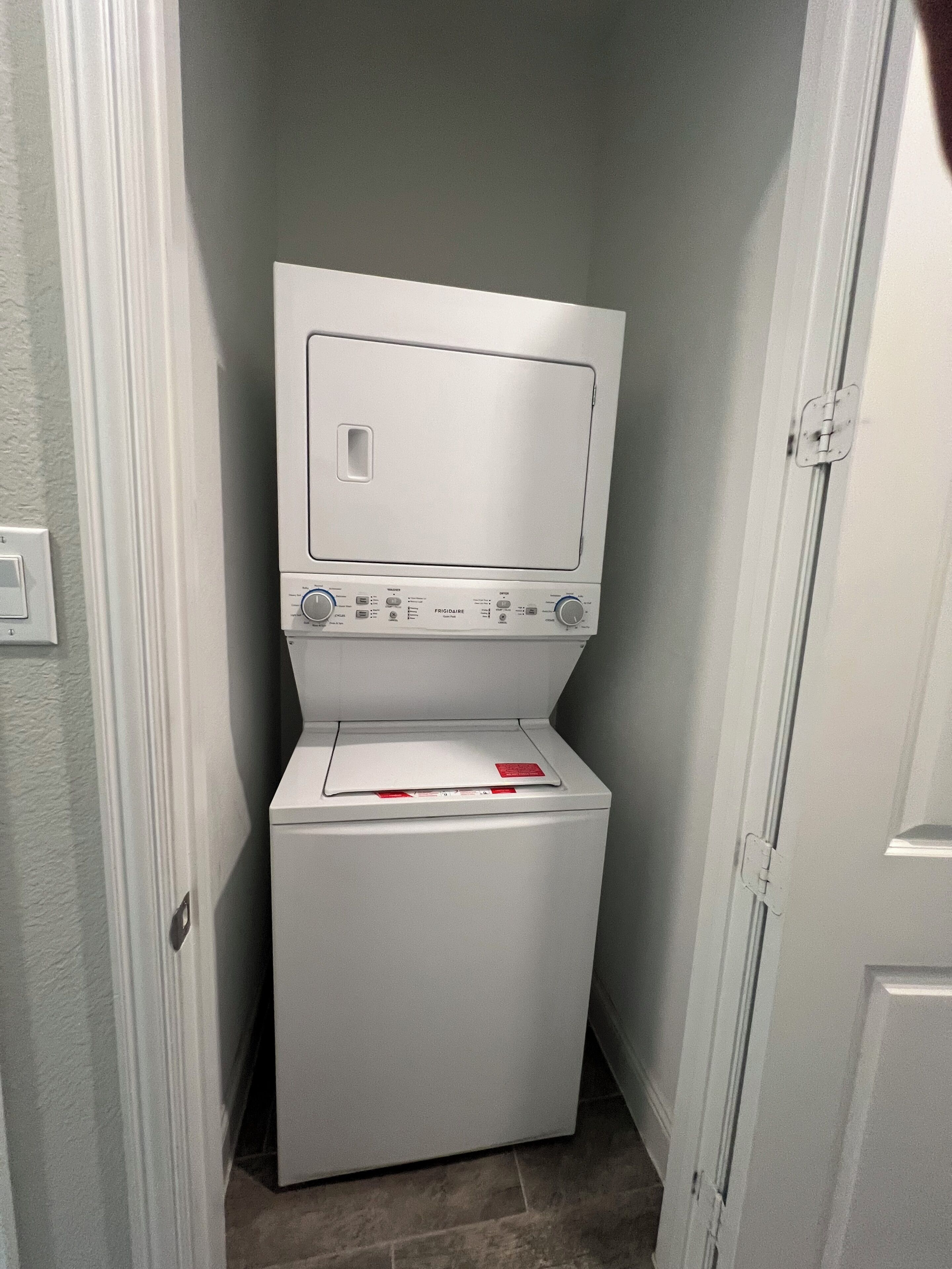 A compact, white laundry room with a front-loading washer and dryer, a small window, and a door to the right.