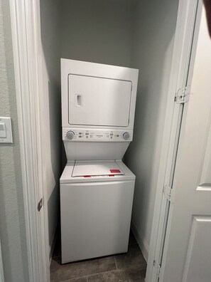 A compact, white laundry room with a front-loading washer and dryer, a small window, and a door to the right.