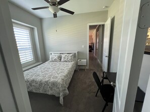 A bedroom with a bed, a ceiling fan, a nightstand, a chair, and a window with blinds.