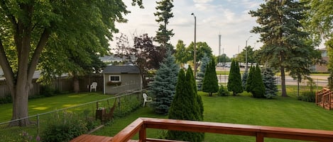 A wooden deck with a view of a well-maintained lawn, a small shed, and a tall tree.