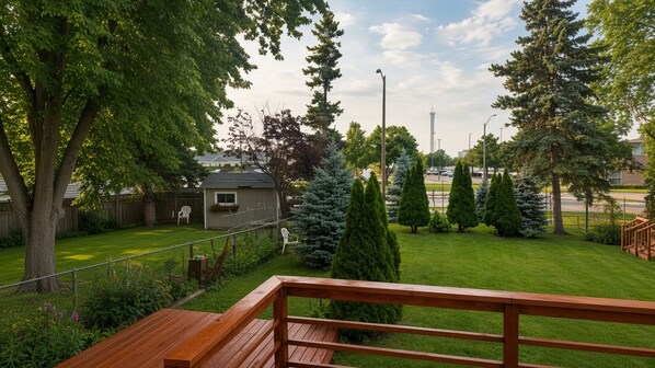 A wooden deck with a view of a well-maintained lawn, a small shed, and a tall tree.