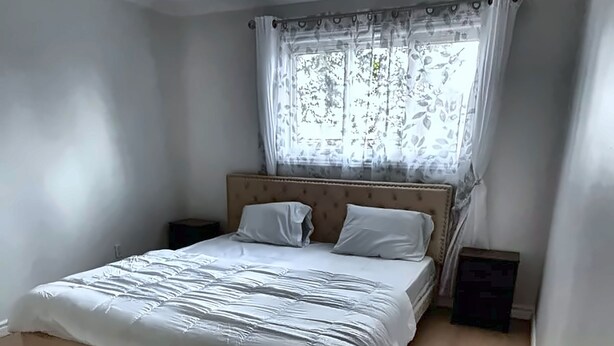 Un dormitorio con cama, ventana con cortina y suelo de madera.