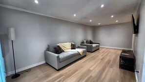 A modern living room with two grey sofas, a flat-screen TV mounted on the wall, and a wooden floor.