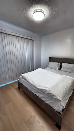Een slaapkamer met een bed, hoofdbord, een plafondlamp en een raam met zonwering.