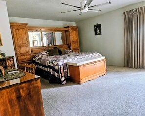 A bedroom with a bed, a wooden dresser, a desk, a chair, a ceiling fan, and a window with curtains. - Forest mountain retreat with resort-style amenities and minutes from Sisters (Sisters)