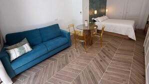 Ein modernes Hotelzimmer mit einem blauen Sofa, einem runden Esstisch mit Stühlen, einem Bett und einem großen Spiegel an der Wand.
