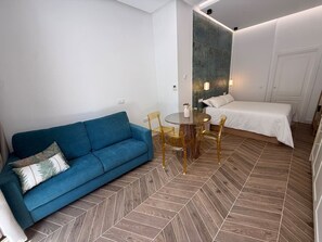 A modern hotel room with a blue sofa, a round dining table with chairs, a bed, and a large mirror on the wall. - La Casona de les Arts 2 - Oceanográfic (València)