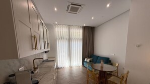 Eine moderne Küche mit Einbauofen, eine Essecke mit rundem Tisch und Stühlen sowie ein Wohnbereich mit Sofa und Vorhängen.