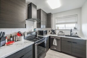 Una cocina moderna con armarios oscuros, una estufa de acero inoxidable, un microondas y un horno empotrado.