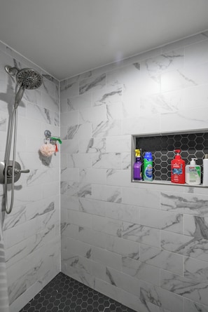 A bathroom with a shower, marble tiles, and a shelf with toiletries.