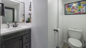 A bathroom with a white sink, dark vanity, a mirror, a toilet, and a colorful abstract painting on the wall.