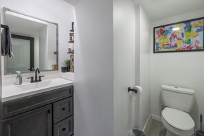 A bathroom with a white sink, dark vanity, a mirror, a toilet, and a colorful abstract painting on the wall.