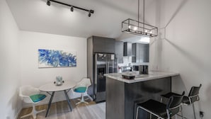 A compact kitchen with a central island, a refrigerator, and a microwave. There is a dining area with two chairs and a small table.
