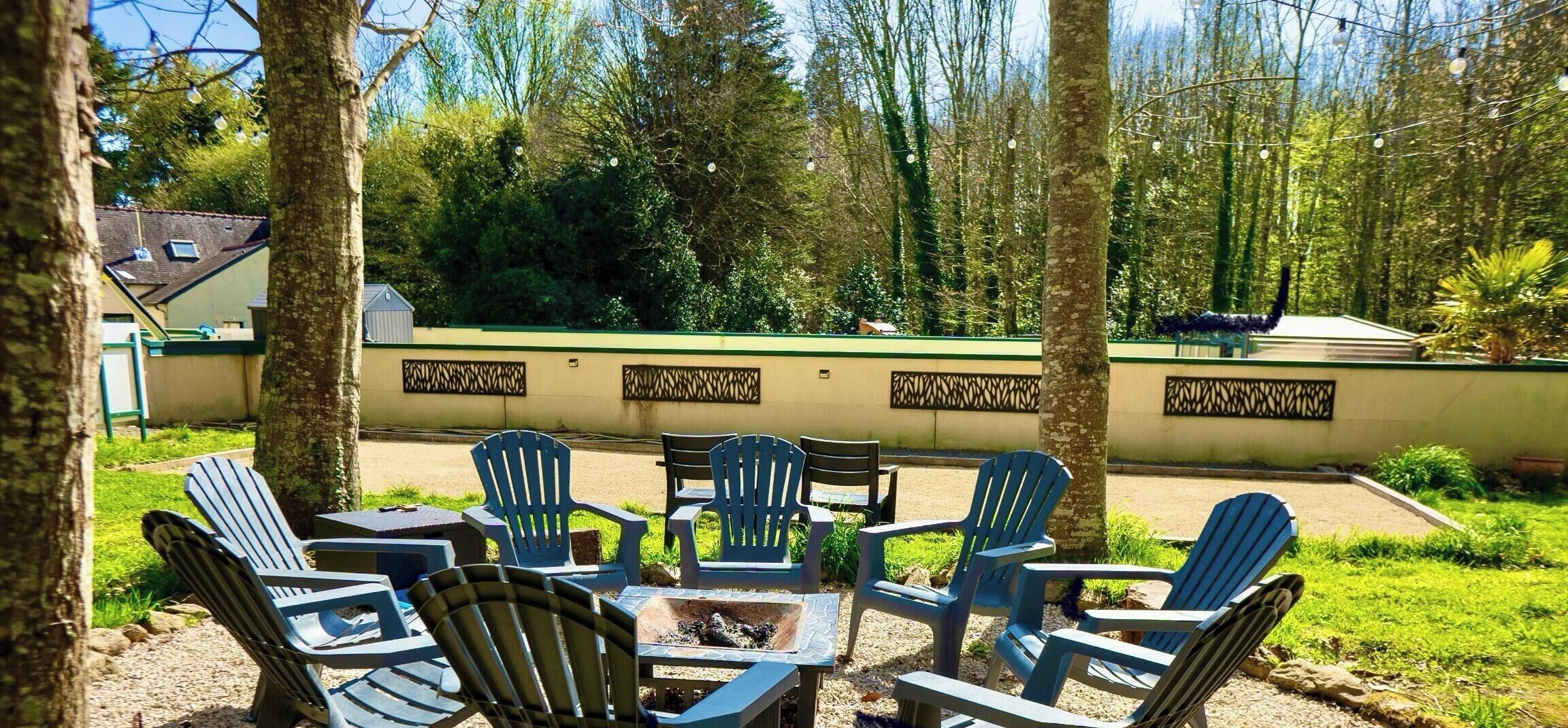 Un espace extérieur aménagé avec des chaises et une table, entouré d’arbres et d’un mur végétal.
