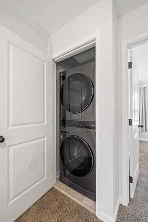 Une buanderie équipée de deux machines à laver et deux sèche-linge à chargement frontal, placés l’un sur l’autre.