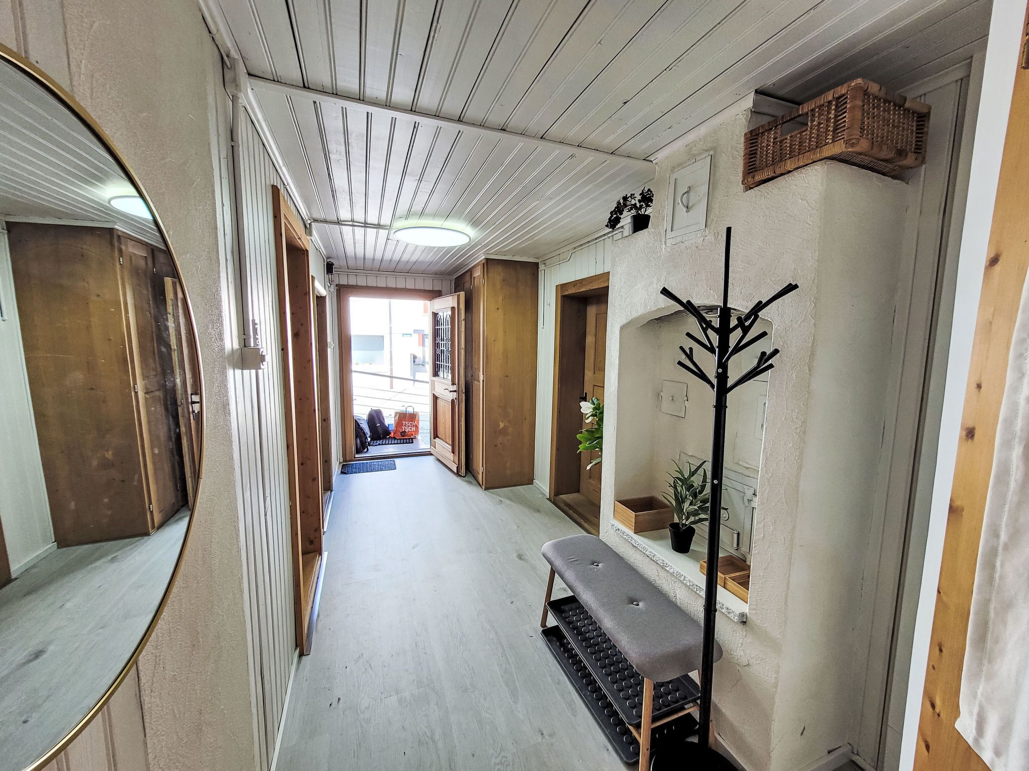Un couloir avec des lambris en bois, un banc, un porte-manteau et une plante en pot.