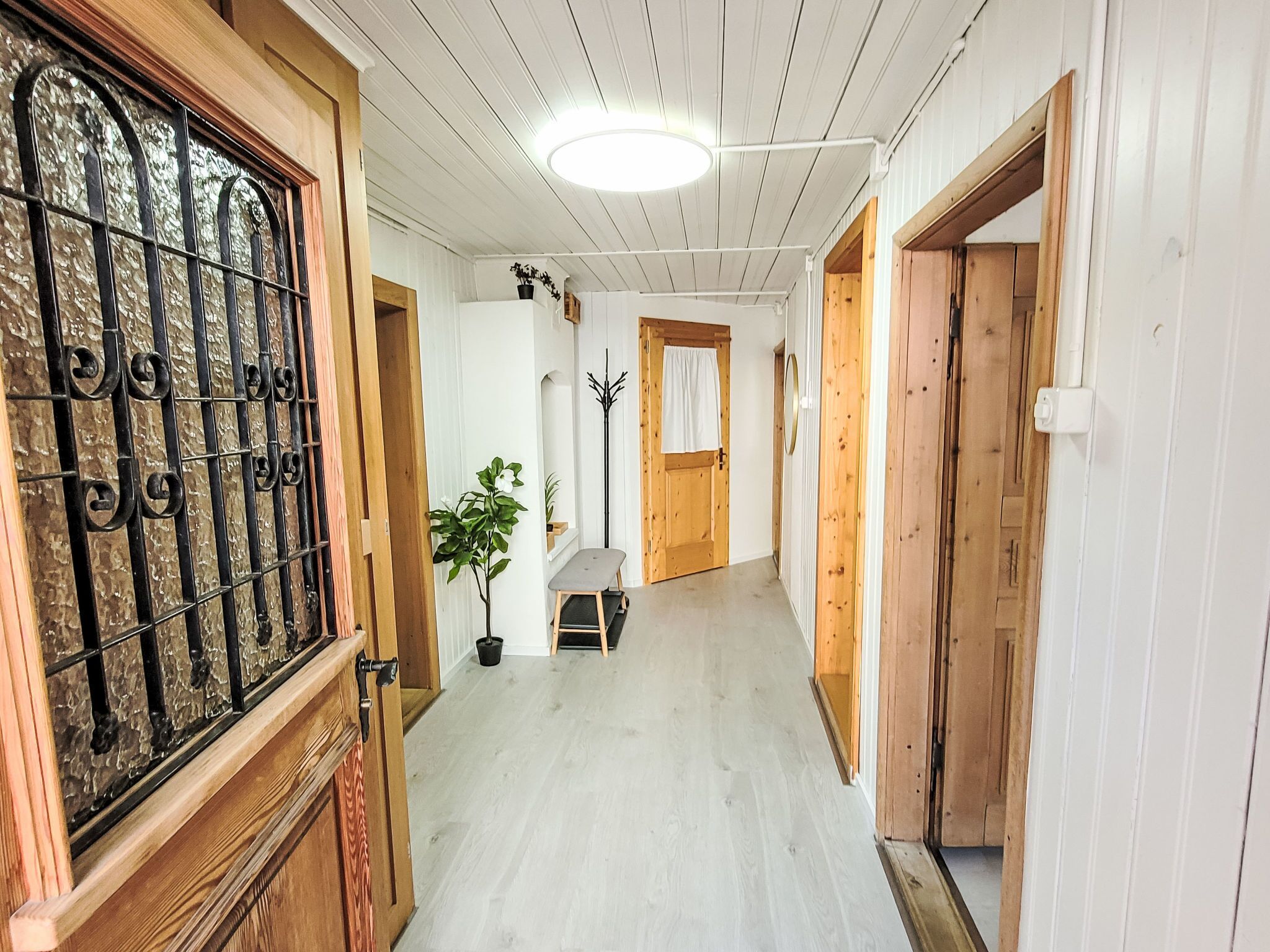 Un couloir avec des portes en bois, une plante en pot et un banc.