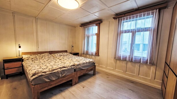 Et soveværelse med en træseng, to sengeborde, et natbord, et vindue med gardiner og en loftslampe.