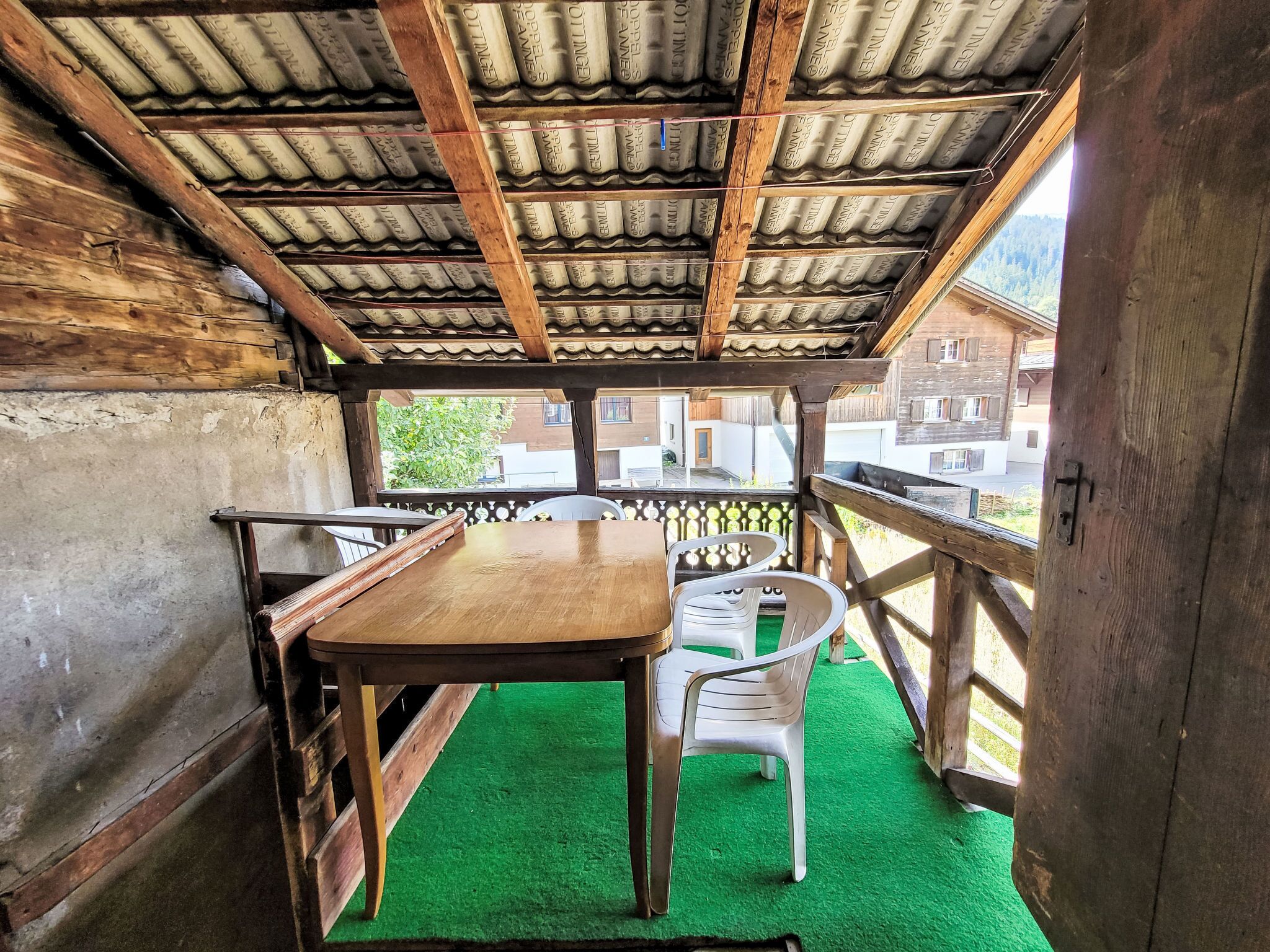 Une structure rustique en bois, avec un toit en tuiles, une table en bois et des chaises en plastique.