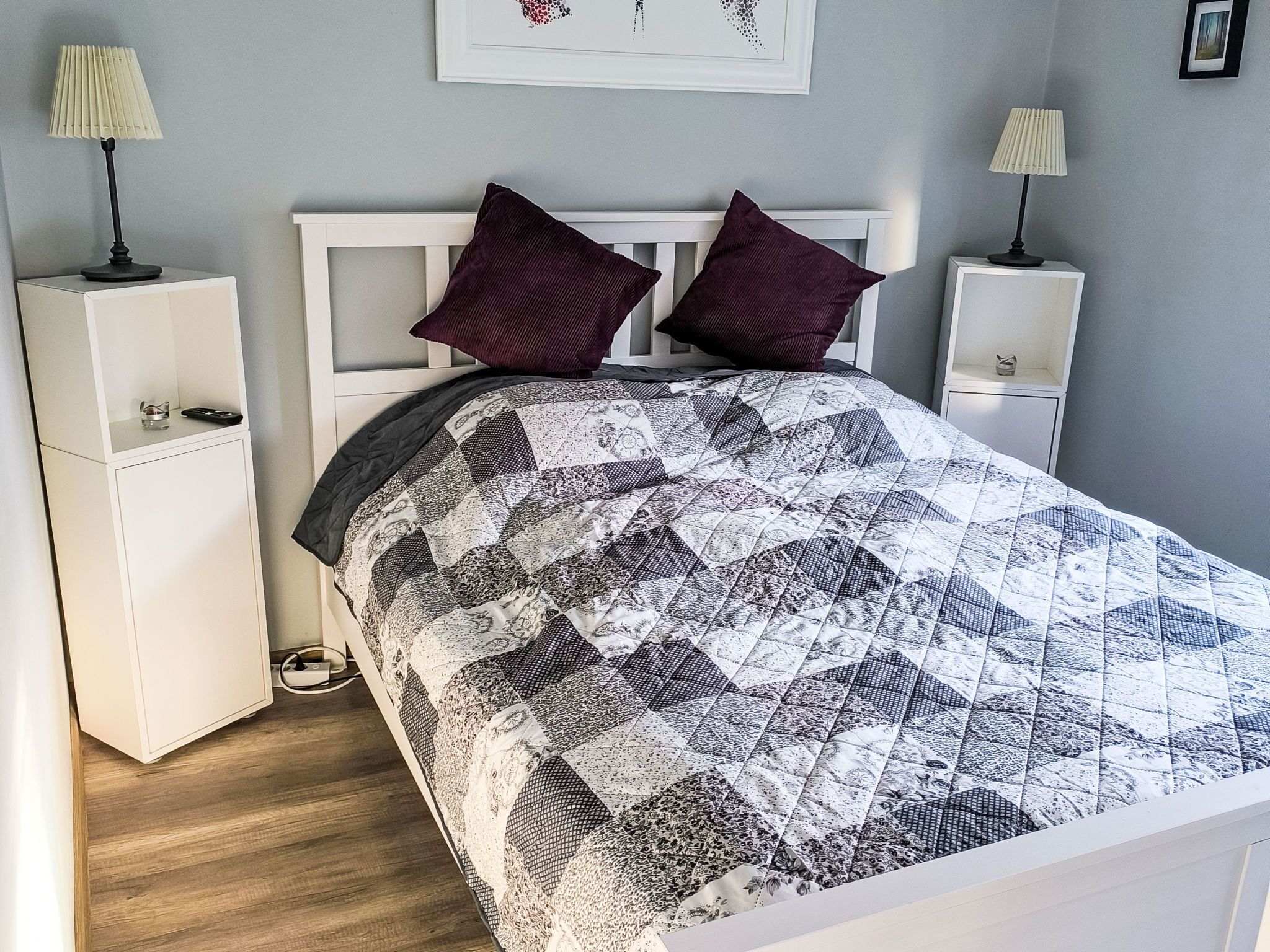 A bedroom with a bed, two nightstands, a lamp on each nightstand, and a wall-mounted picture.