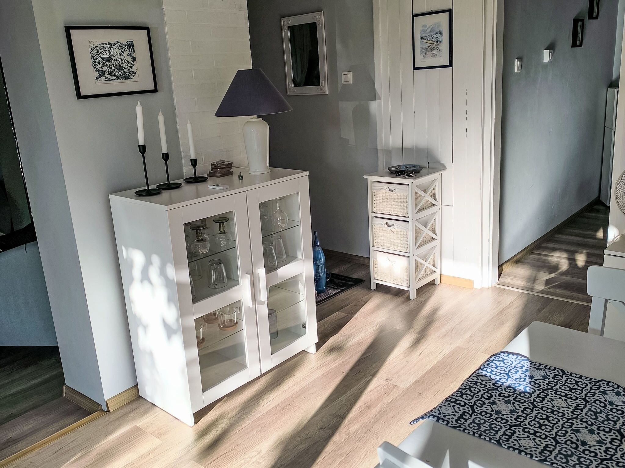 Ett rum med ett vitt skåp med glasdörrar, en lampa och inramade konstverk på väggen.