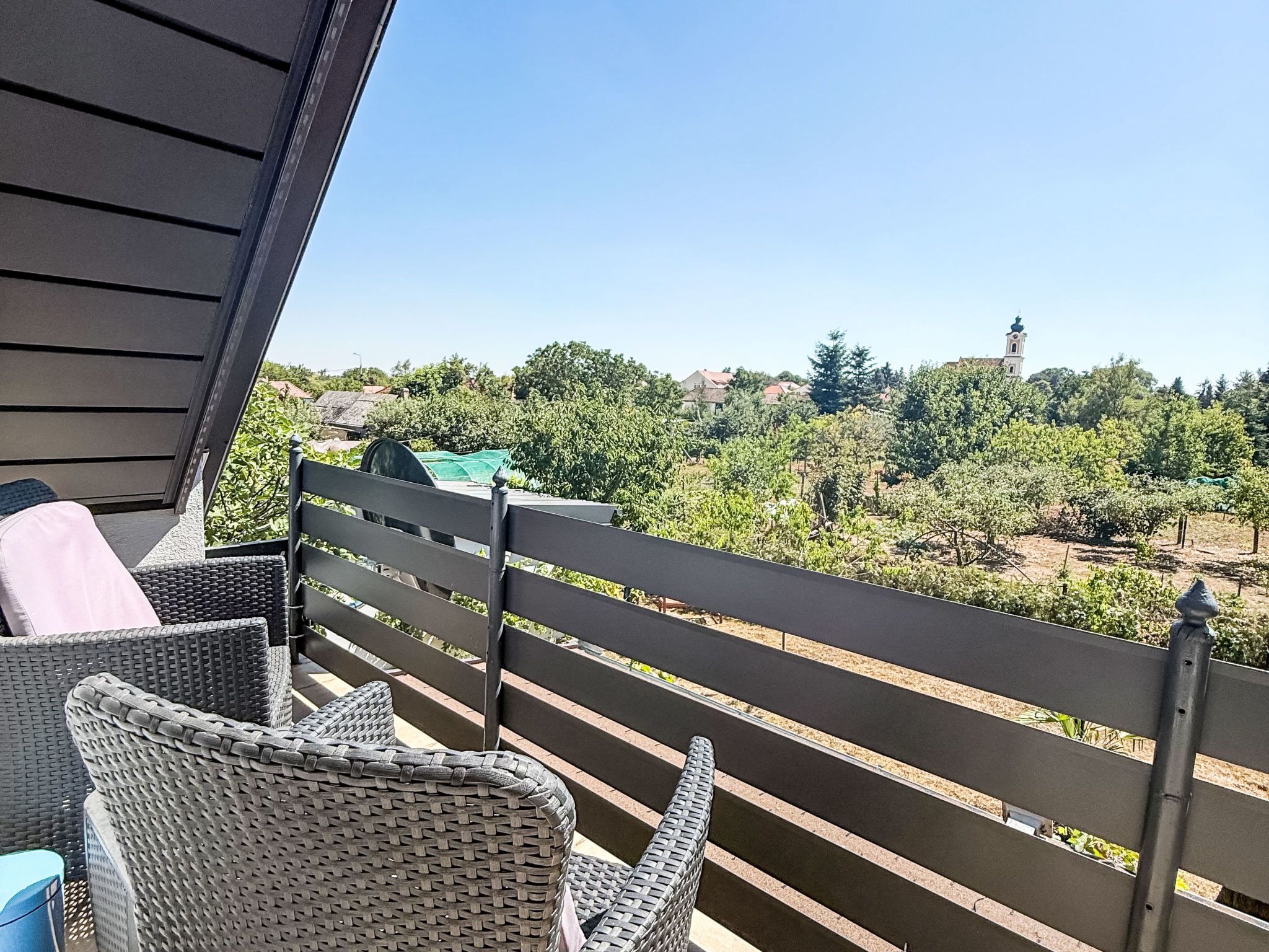 A balcony with wicker furniture and a view of a vineyard and a church tower.