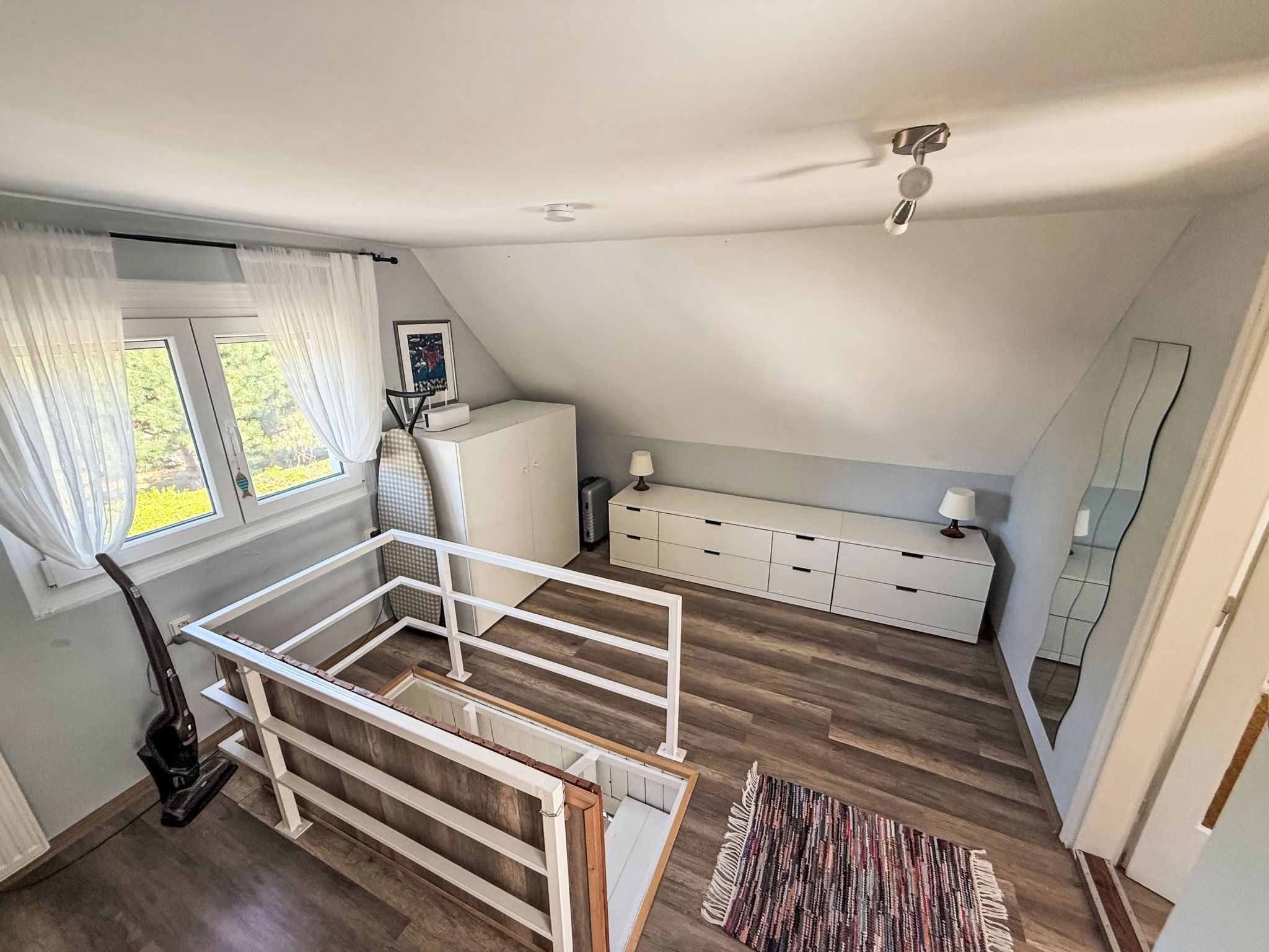 A room with a loft bed, a desk, a radiator, and a window with curtains.