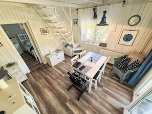 A room with a wooden floor, a dining table with chairs, a staircase, a window with curtains, and a clock on the wall. - Babaház by Interhome (Balatonmariafurdo)