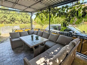 An outdoor patio with a table and seating, surrounded by greenery and a car in the background. - Babaház by Interhome (Balatonmariafurdo)