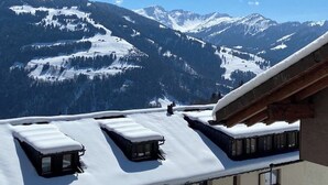Un bâtiment doté de nombreuses fenêtres et d’un toit plat recouvert de neige, qui offre une vue sur des montagnes aux sommets enneigés.