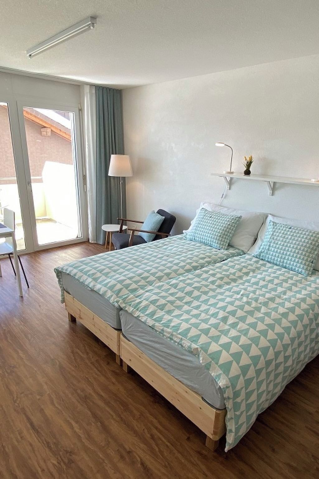 Ein Schlafzimmer mit Bett, Sessel, Schreibtisch und Lampe.