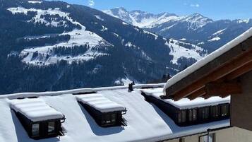 Un edificio con múltiples ventanas y un techo plano cubierto de nieve, con vistas a una cadena montañosa nevada.