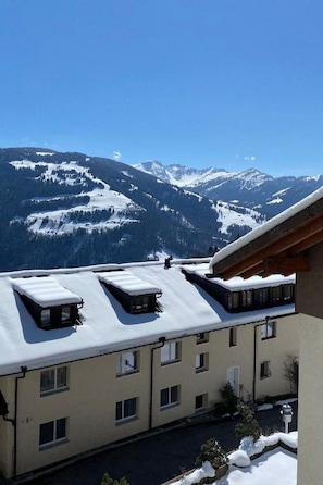 Un edificio con múltiples ventanas y un techo plano cubierto de nieve, con vistas a una cadena montañosa nevada.