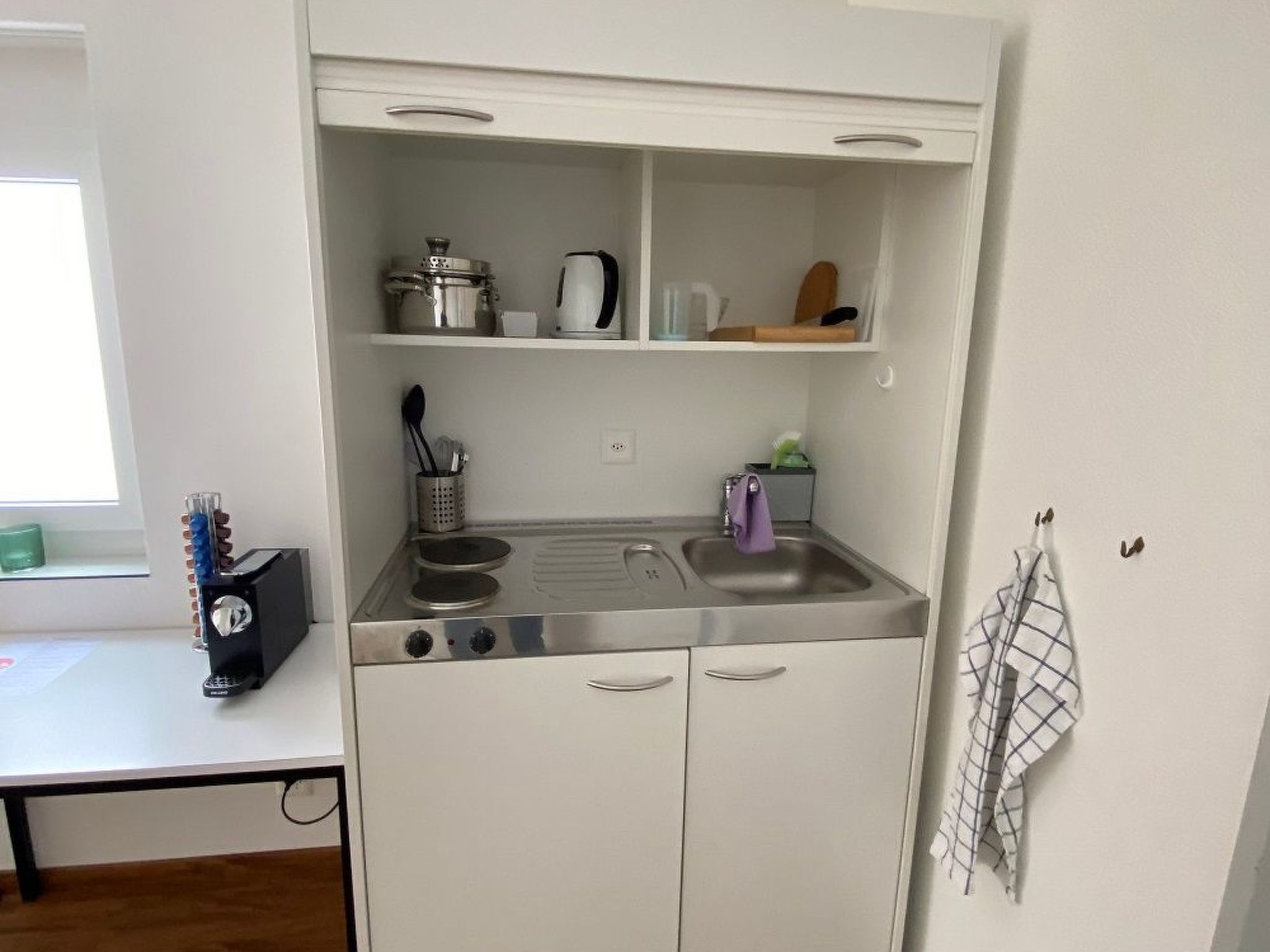A compact kitchenette with a stove, sink, and storage shelves.