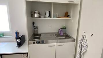 A compact kitchenette with a stove, sink, and storage shelves.