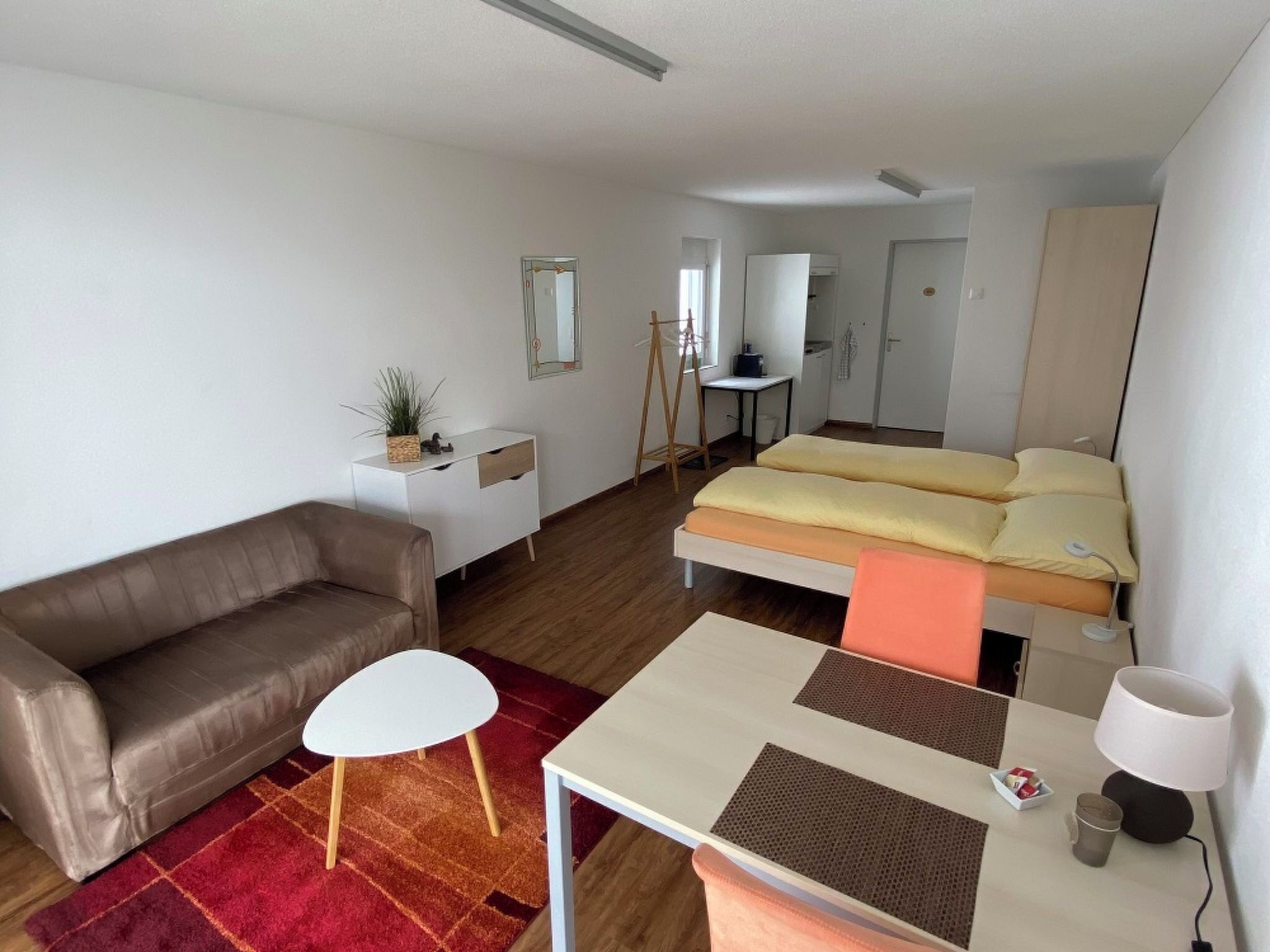 A compact hotel room with a single bed, a sofa, a small table, and a desk.