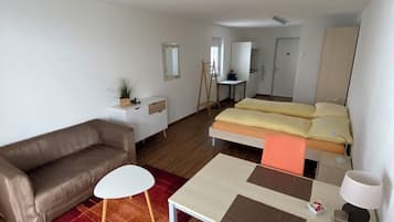 A compact hotel room with a single bed, a sofa, a small table, and a desk.