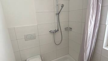 Ein kleines Badezimmer mit Fliesen, einer Dusche, einer Toilette und einer Bedienkonsole.