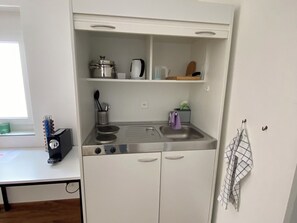 A compact kitchenette with a stove, sink, and storage shelves.