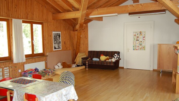 Ein Holzinnenraum mit Esstisch, Stühlen, einer Couch und einem Spielbereich mit Spielzeug.