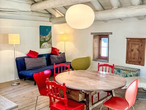 A dining area with a round wooden table, red chairs, a blue sofa with patterned cushions, a floor lamp, and a painting on the wall. - Casa Rederer by Interhome (Bondo)